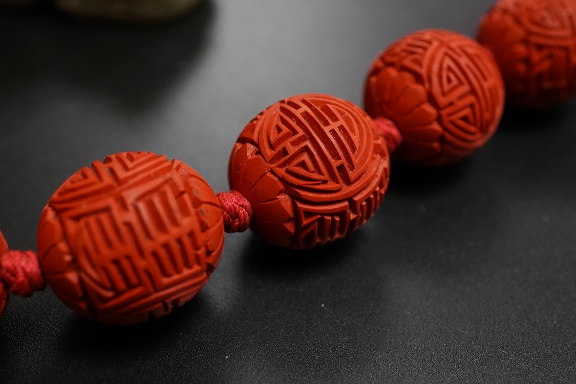 A Chinese red lacquered bead necklace and a bowenite jade figure of a cat